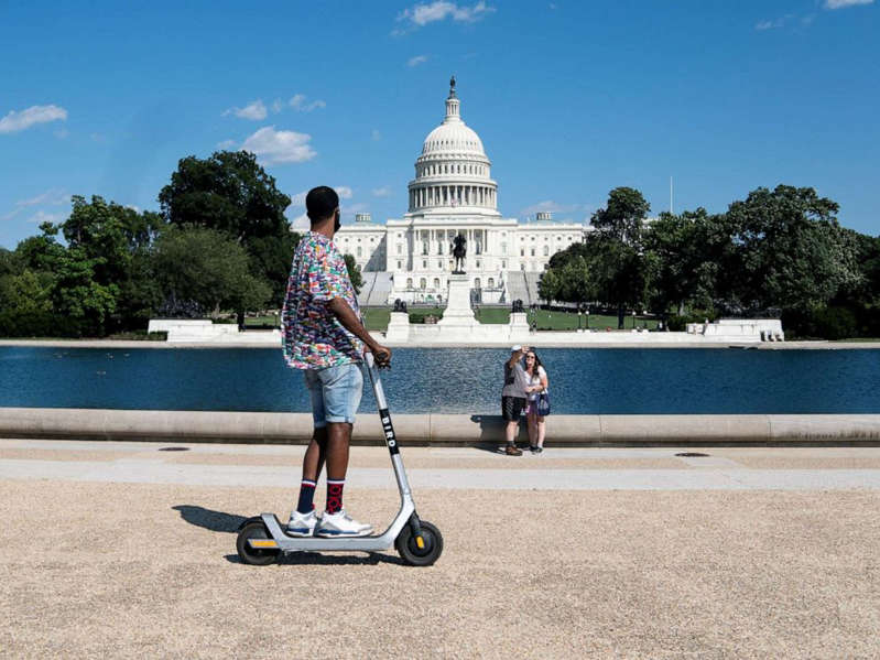a young boy riding a skateboard up the side of a road: People are seen near the Capitol building, Sept. 6, 2021.